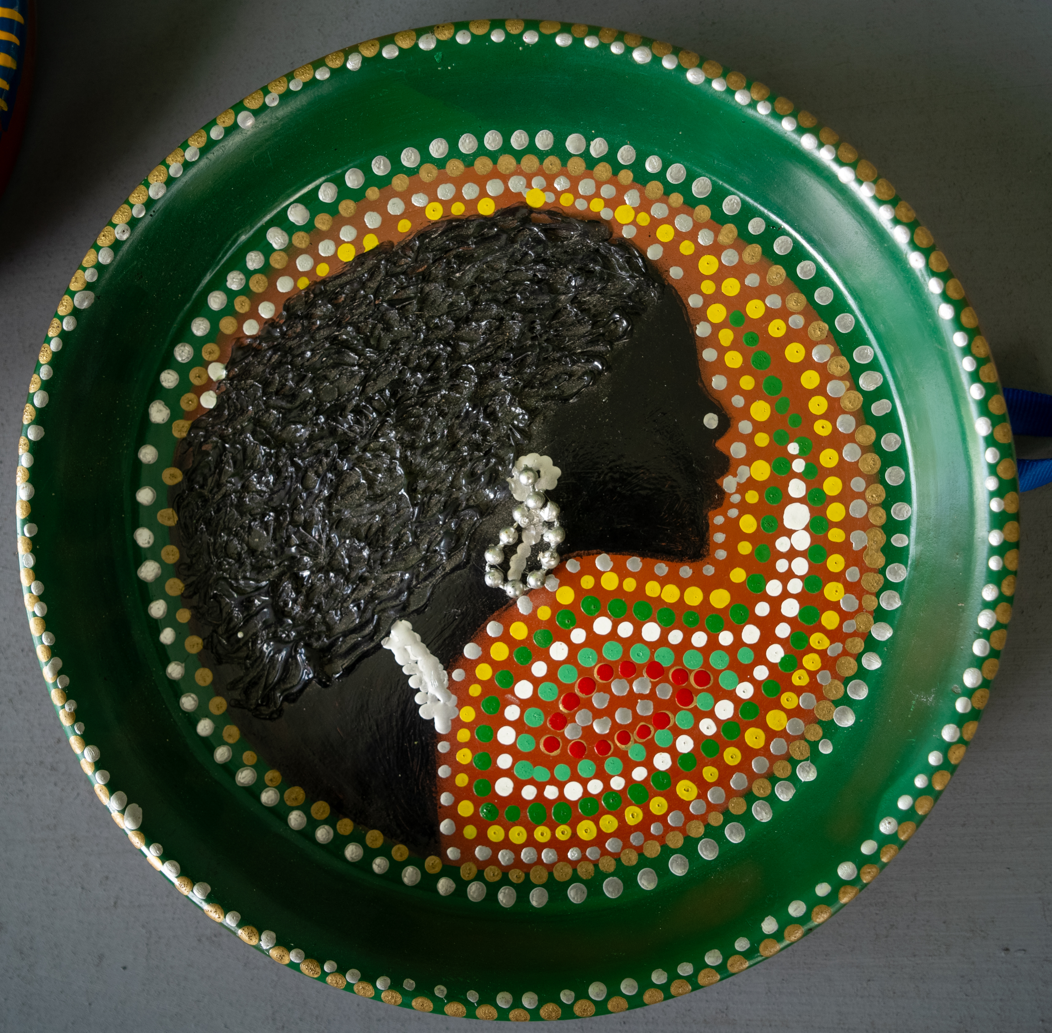 Circular green relief portrait in profile with textured hair and dotted garments